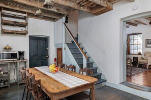 Un comedor con mesa de madera, sillas, frutero, cafetera y una escalera.
