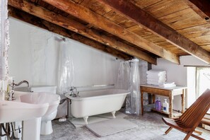 Un baño rústico con una bañera blanca, un lavamanos y un techo de madera.