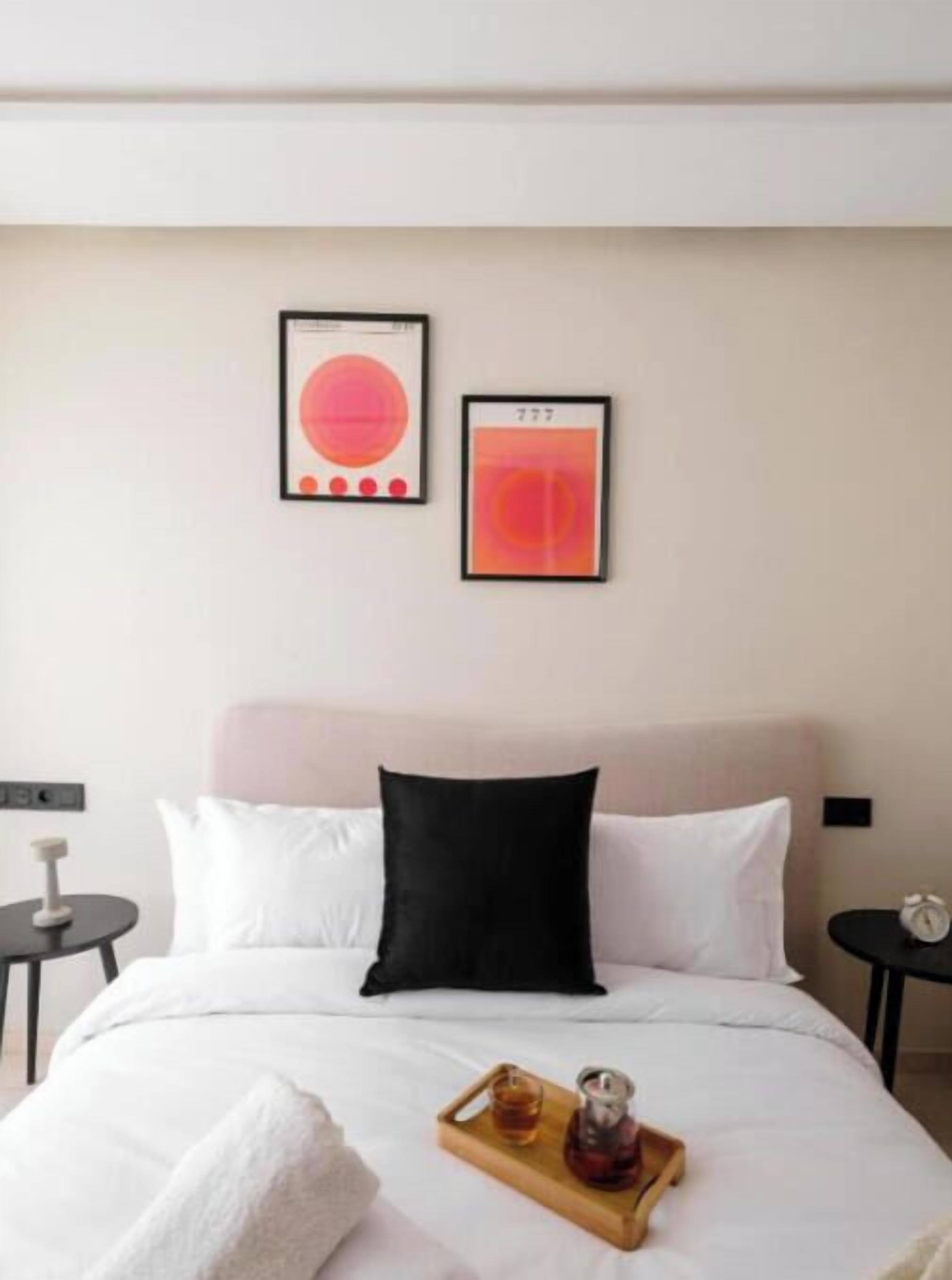 Een hotelkamer met een bed, een dienblad met een drankje en twee kunstwerken in lijsten aan de muur.