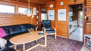 Ein gemütliches Blockhaus-Interieur mit Holzbalkendecke, einem schwarzen Ledersofa, einem Holztisch und einem gemusterten Teppich.
