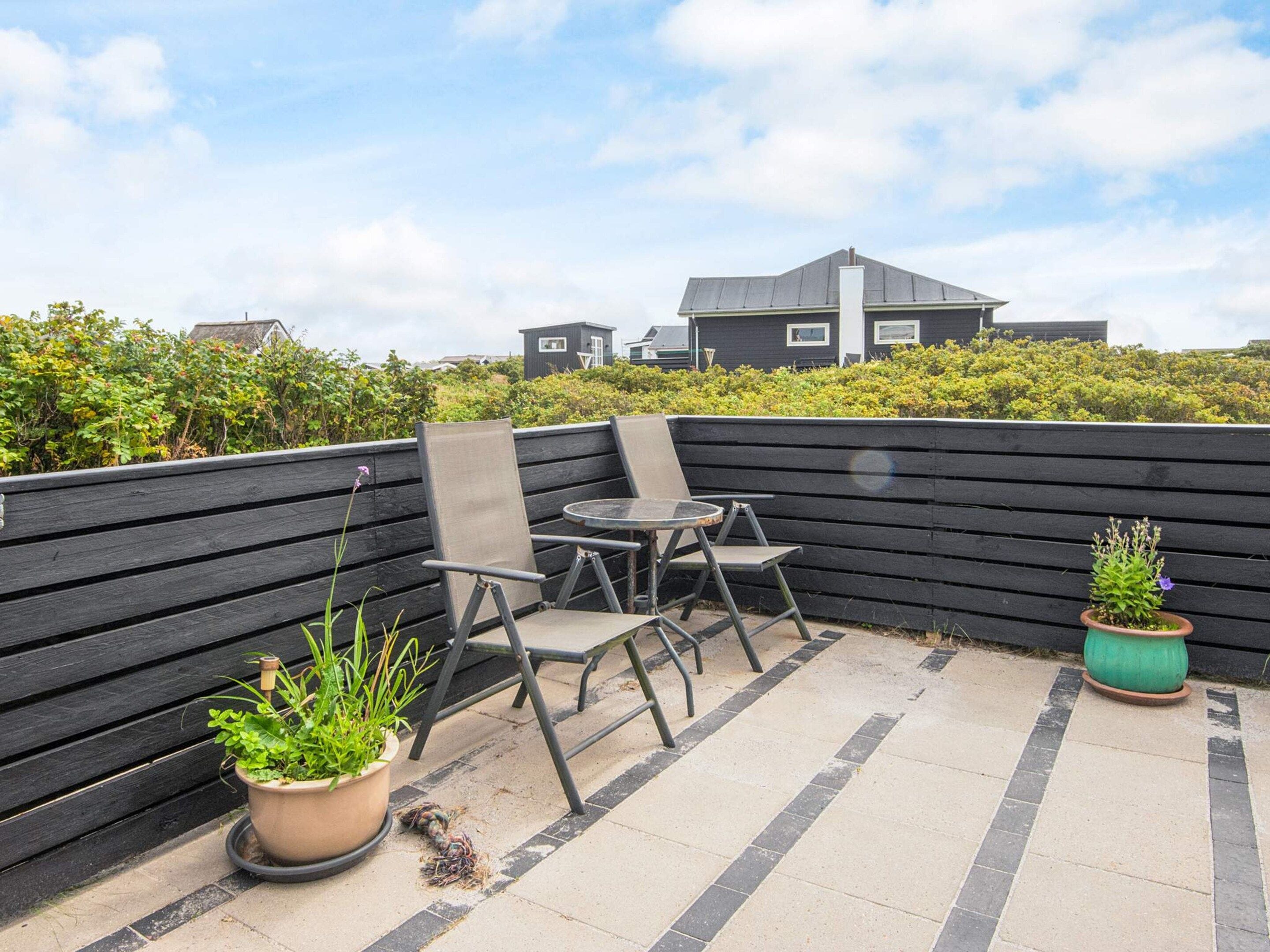 A rooftop terrace with a table and chairs, potted plants, and a view of a building in the background.
