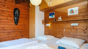 Ein Holzhüttenraum mit zwei Betten, einer Wandmaske und Kinderzeichnungen.