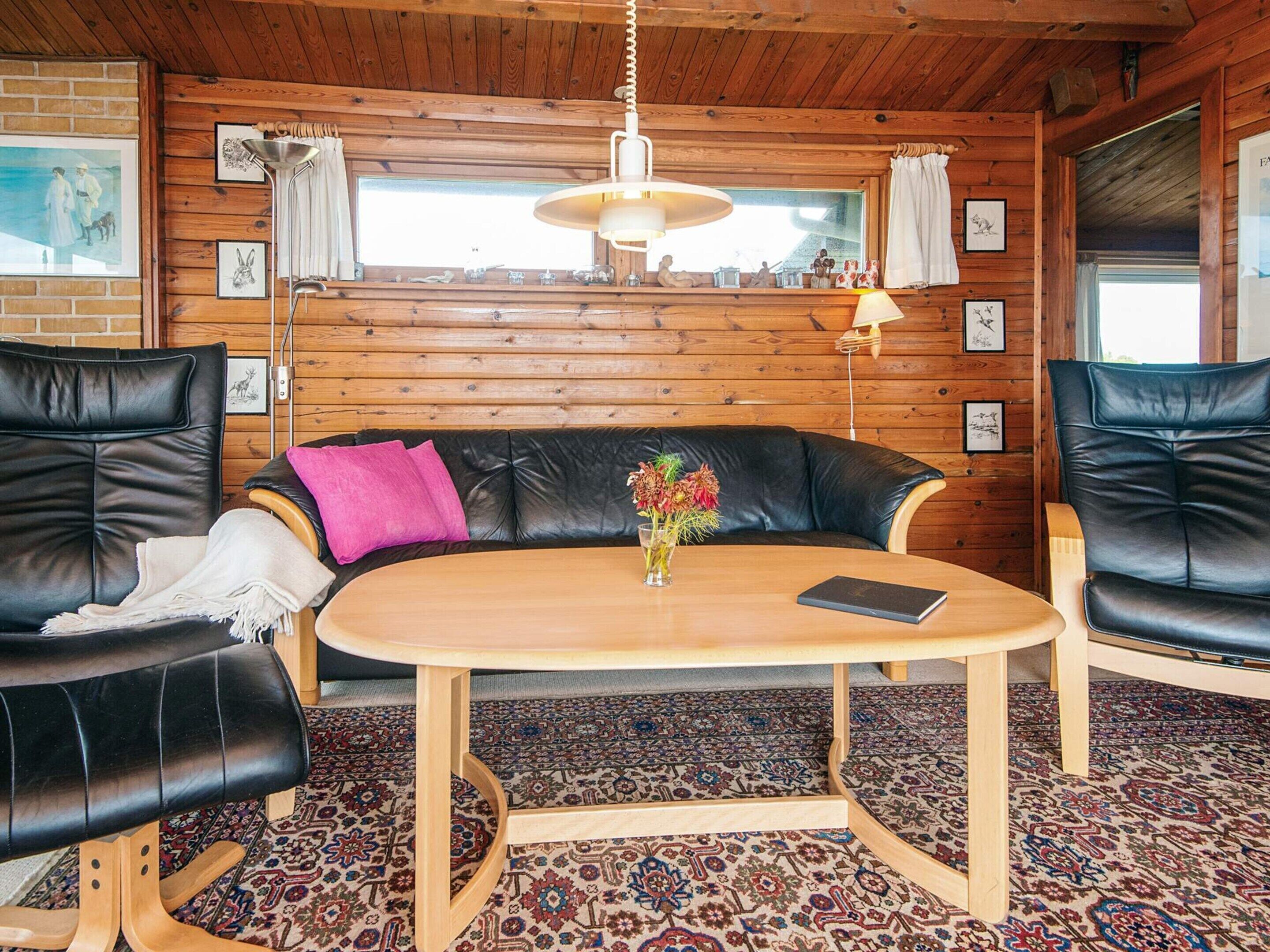 Ett mysigt rum med träinredning, en svart lädersoffa, ett träbord och en mönstrad matta.