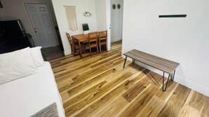 Huone, jossa on sänky, puinen ruokapöytä tuoleineen, penkki ja ovi.