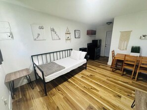 Ein Zimmer mit einem Bett, einem Fernseher, einem Esstisch und einer kleinen Küchenzeile.