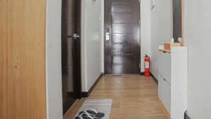 Un pasillo estrecho con una puerta de madera, un extintor y un espejo en la pared derecha.