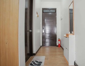 A narrow hallway with a wooden door, a fire extinguisher, and a mirror on the right wall. - Serene Stay at Paseo Verde (Las Piñas)