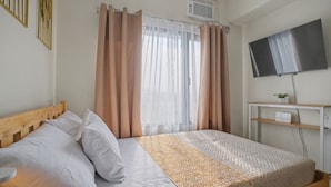Un dormitorio con cama, cortinas, televisor, una estantería con una planta y un aire acondicionado instalado en la pared.