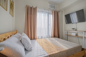 A bedroom with a bed, curtains, a TV, a shelf with a plant, and a wall-mounted air conditioner. - Serene Stay at Paseo Verde (Las Piñas)