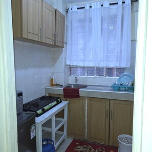 A compact kitchen with a gas stove, a sink, and a window with white curtains. - Cutie Suites TRM | Fast Wi-Fi • Netflix • Parking (Nairobi)