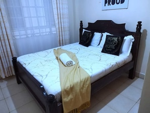 A bed with a headboard, a rolled towel, and pillows with 'HOME SWEET HOME' text. - Cutie Suites TRM | Fast Wi-Fi • Netflix • Parking (Nairobi)