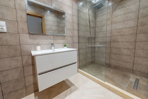 A bathroom with a glass shower enclosure, a white vanity with a mirror, and a small potted plant. - Magnifique Appartement au Golf (El Mouradia)