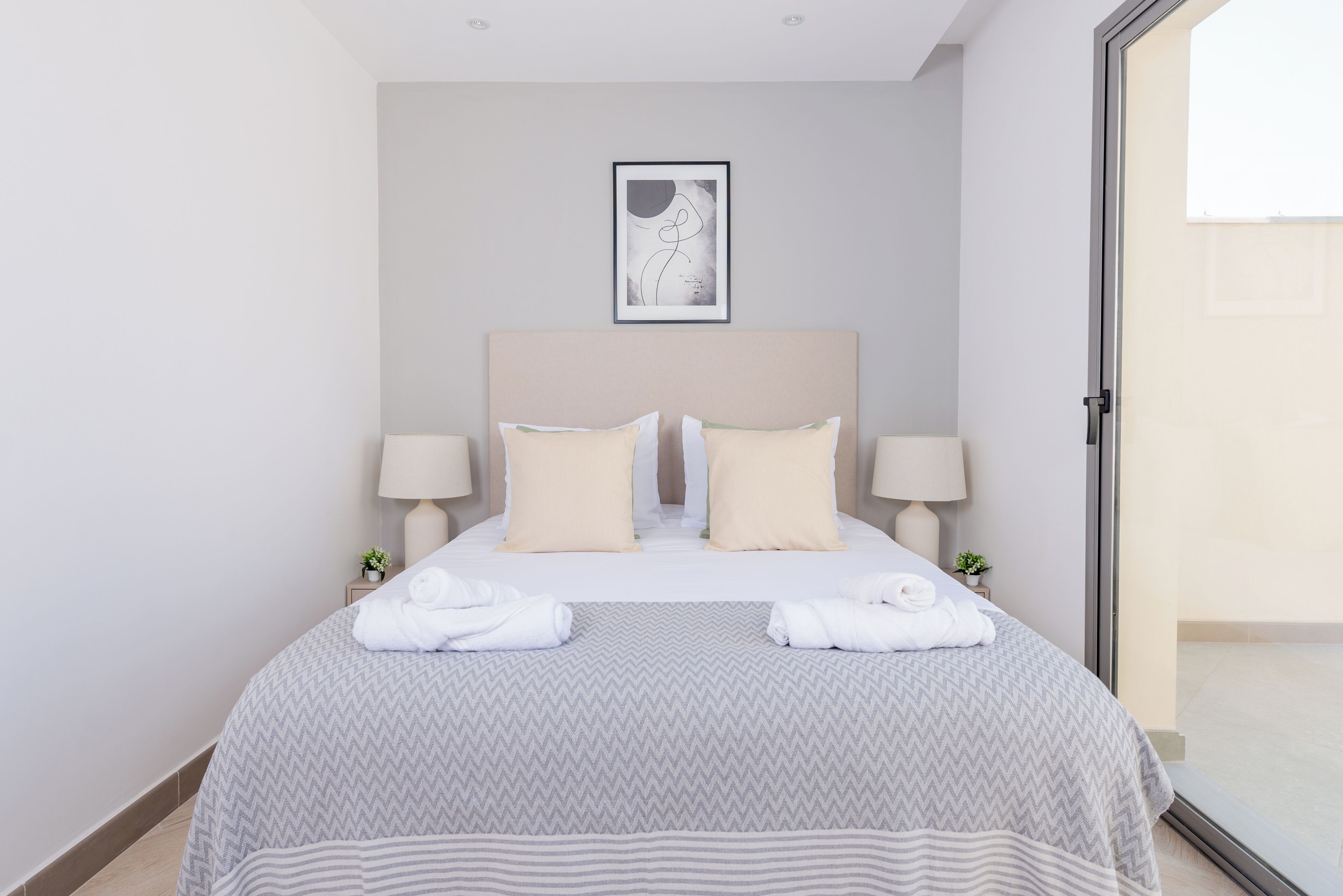 Une chambre d’hôtel avec un lit, deux lampes de chevet, une œuvre d’art encadrée au-dessus du lit et une vue à travers une porte vitrée.