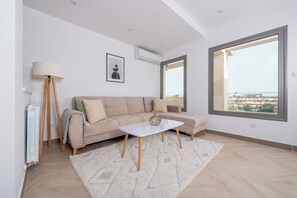 A modern living room with a sofa, a coffee table, a floor lamp, and a large window. - Magnifique Appartement au Golf (El Mouradia)
