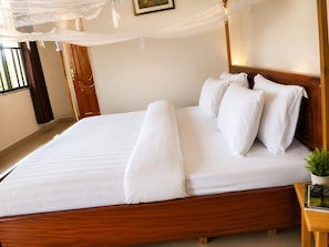 A neatly made bed with white linens, a wooden headboard, and a bedside table with a remote control and a potted plant.