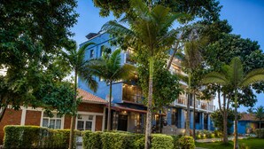Un hotel de varios pisos con fachada azul, un camino pavimentado y abundante vegetación.