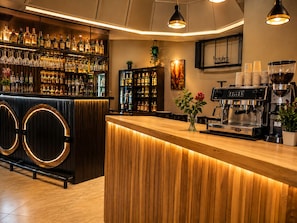 Un espace bar avec un comptoir en bois, des étagères remplies de bouteilles d’alcool, un appareil à café et une plante en pot.