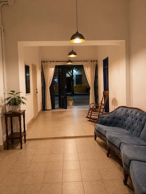 A room with a sofa, a small table with a plant, a hanging light fixture, and a view of the outside.