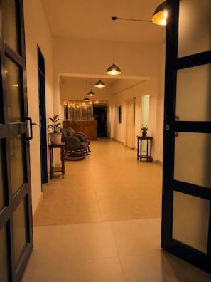 A hallway leading to a seating area with a reception desk, potted plants, and pendant lighting.