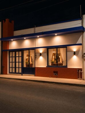A building with a brick facade, large windows with curtains, and exterior lighting.