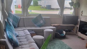 Una sala de estar con un sofá modular, un televisor, una mesita y una alfombra verde.