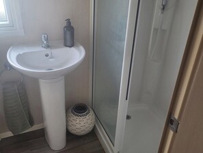 Ein Badezimmer mit einem Standwaschbecken, einer Dusche mit Glastür und einer Zierflasche.