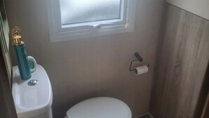 Un baño pequeño y funcional con inodoro, lavabo y ventana sobre el inodoro.