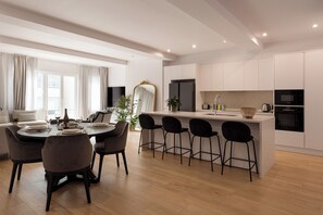 Eine moderne Küche mit weißen Schränken, einer zentralen Kochinsel mit Barhocker und einem Essbereich mit rundem Tisch und Stühlen.