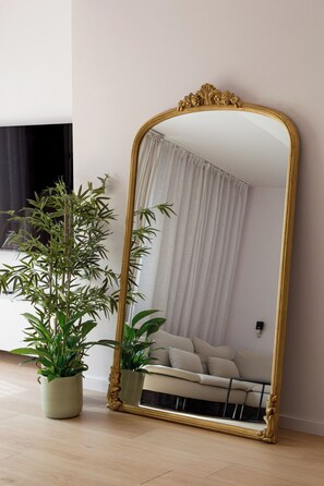 Ein Zimmer mit einem großen, verzierten Spiegel, einem Blumentopf und einem Sofa.