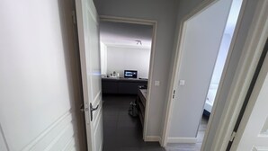En smal hall som leder till ett rum med en säng och ett skrivbord.