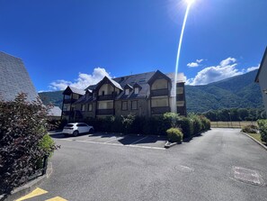 A multi-story building with a parking lot in front, surrounded by greenery and a mountain in the background.