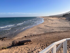 Une plage avec une rambarde en bois, un rivage sablonneux et des vagues.