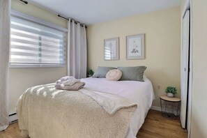 A bedroom with a bed, a window with blinds, a small round table with a plant, and two framed pictures on the wall. - Spa & Sauna - Chalet de l'Ours noir (Notre-Dame-des-Bois)