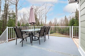 A covered patio with a table and chairs, a white railing, and a view of trees and a house. - Spa & Sauna - Chalet de l'Ours noir (Notre-Dame-des-Bois)