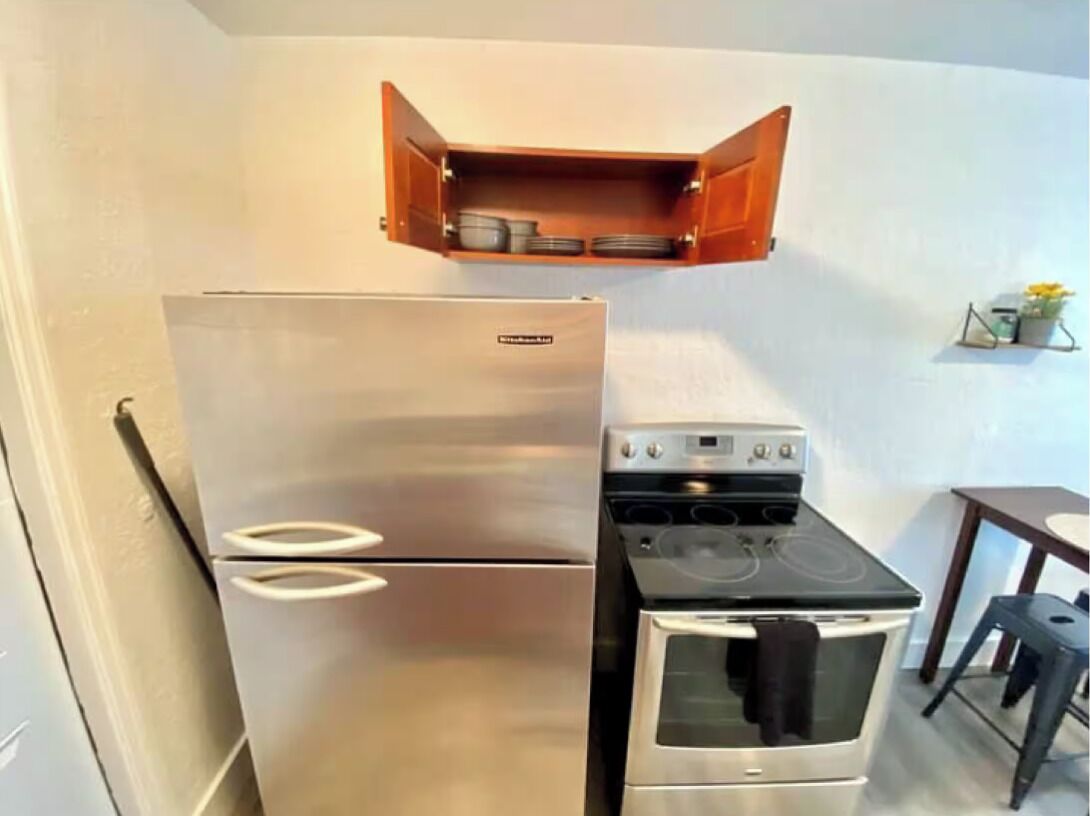 Une cuisine compacte équipée d’un réfrigérateur en acier inoxydable, d’une cuisinière et d’un meuble en bois placé au-dessus de la cuisinière.