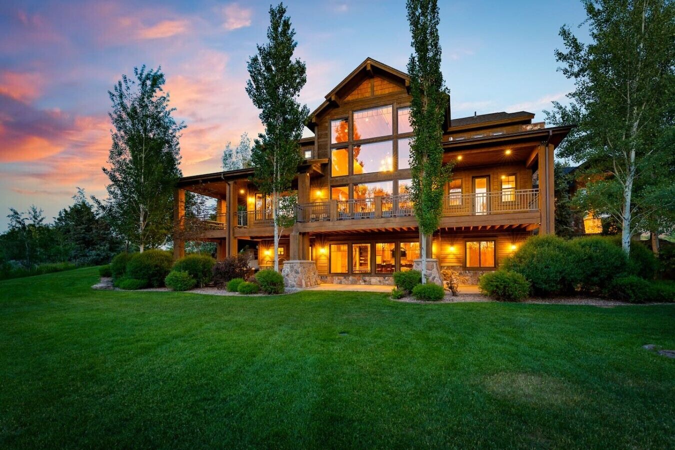 A large, multi-story wooden house with a balcony, surrounded by a well-maintained lawn and trees.