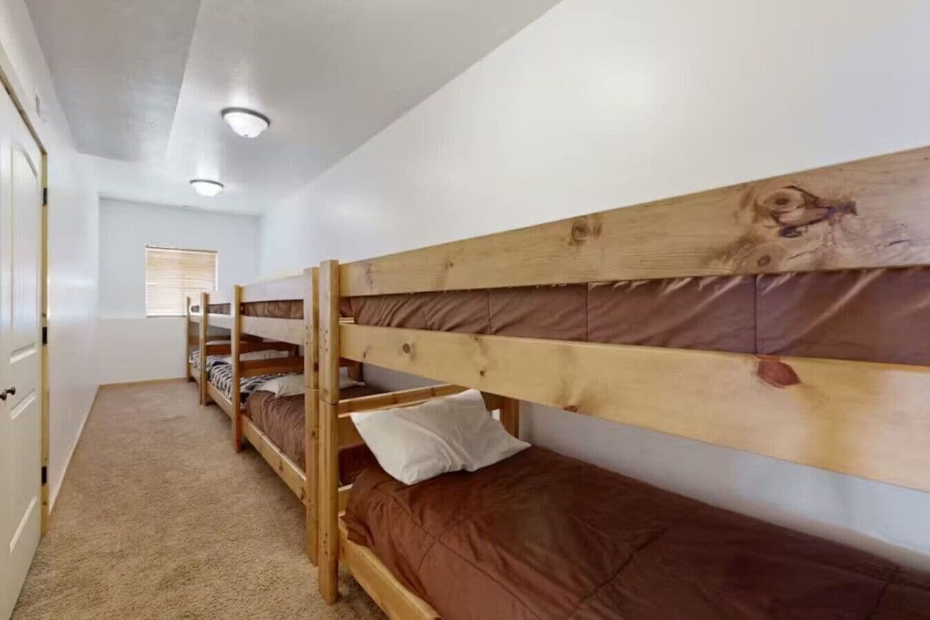 A room with bunk beds, a door, and a window with blinds.