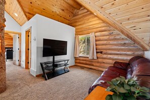 A log cabin interior with a television on a stand, a leather sofa, and a plant. - Big Bear Cabin | Sleeps 32, Near Marina, Lake Views, AC, Log Cabin! (Garden City)