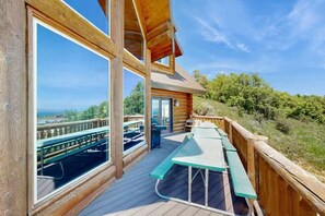 A wooden deck with picnic tables and a view of the landscape. - Big Bear Cabin | Sleeps 32, Near Marina, Lake Views, AC, Log Cabin! (Garden City)