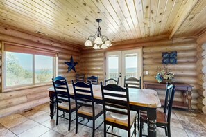 A log cabin interior with a dining table, chairs, a star decoration, and a view through the windows. - Big Bear Cabin | Sleeps 32, Near Marina, Lake Views, AC, Log Cabin! (Garden City)