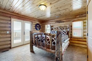 Een slaapkamer in een blokhut met een houten bed, een plafondlamp en uitzicht door de deur.