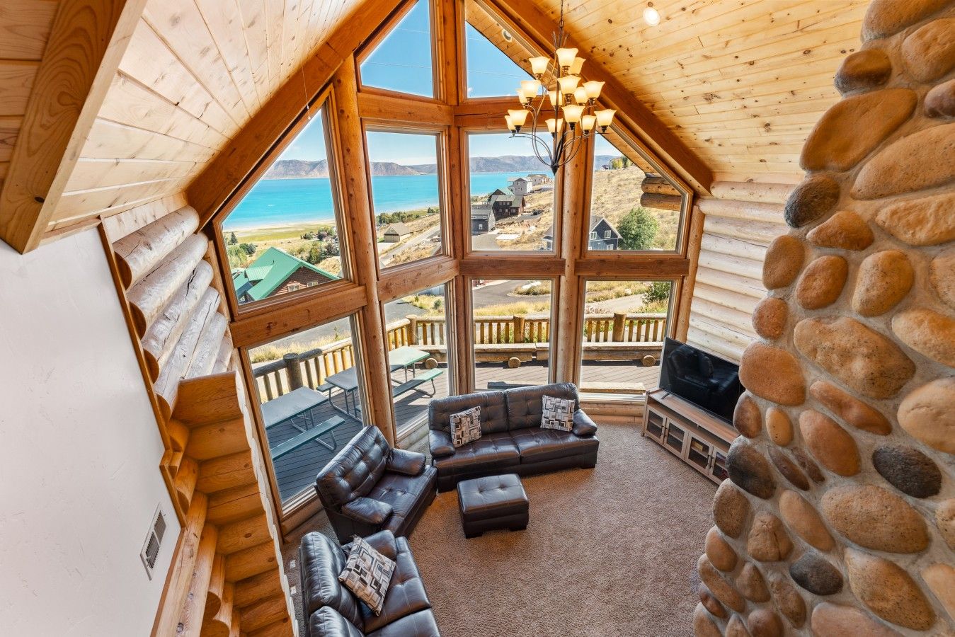 Eine Blockhütte mit einem großen Erkerfenster, einer Steinwand, einem Ledersofa und einem Fernseher.