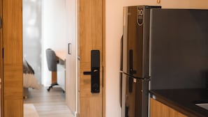 Een moderne keuken met een zwarte koelkast, houten kastjes en een deur naar een slaapkamer met een bed en bureau.