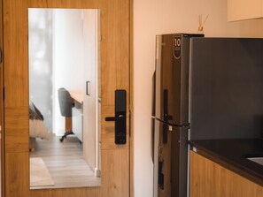 Eine moderne Küche mit einem schwarzen Kühlschrank, Holzschränken und einer Tür zu einem Schlafzimmer mit Bett und Schreibtisch.