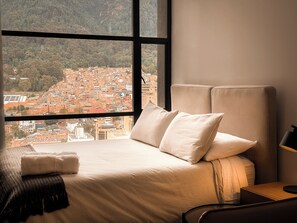 Ein Bett mit Blick auf eine Stadtlandschaft durch ein Fenster.