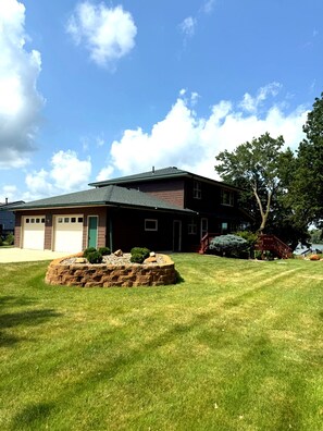 A two-story house with a garage, a stone fire pit, and a well-maintained lawn.
