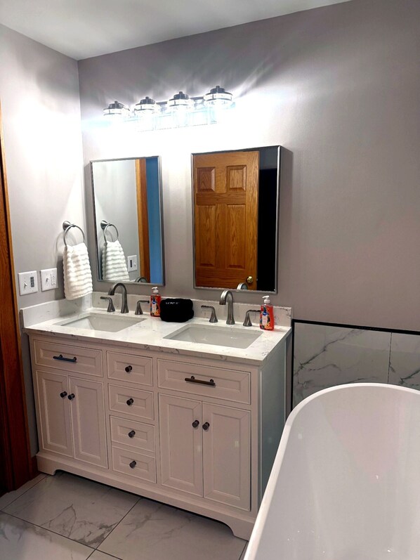 Un baño con tocador doble, un espejo grande, una puerta de madera y una bañera.