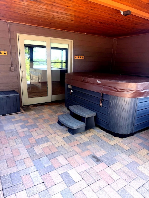 A hot tub area with a wooden ceiling, a sliding glass door, and a brick-patterned patio.