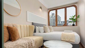 Ein modernes Hotelzimmer mit einer Couch, einem Bett, einem runden Tisch, einer Topfpflanze und einem Fenster mit Blick auf die Stadt.