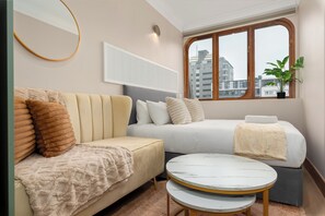 A modern hotel room with a sofa, a bed, a round table, a potted plant, and a window with a city view. - Charlie and the Chairman | Stylish Gem in CBD (Cape Town)